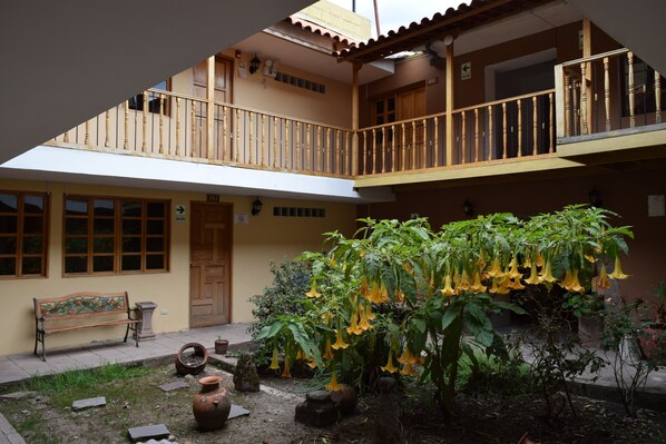 Une cour avec un banc, des plantes en pot et un balcon doté d’une balustrade.