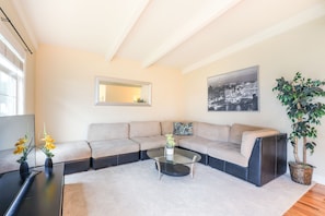 A modern living room with a sectional sofa, a glass coffee table, and a potted plant. - Peaches & Cream (Santa Clara)