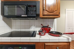 Una cocina con microondas, estufa, una olla roja y una sartén.