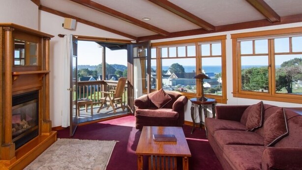 A cozy living room with a fireplace, a large window with a view, and comfortable seating. - Mendocino View West (Mendocino)