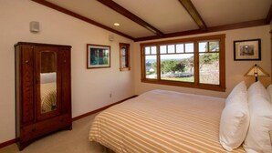 A bedroom with a bed, a wooden wardrobe, a window with a view, and a framed picture on the wall. - Mendocino View West (Mendocino)