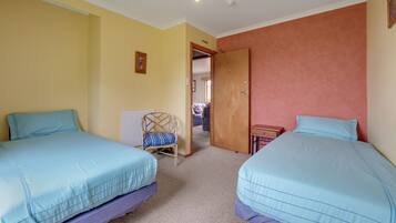 Una habitación con dos camas, una silla, una mesita y una puerta que da a otra estancia.