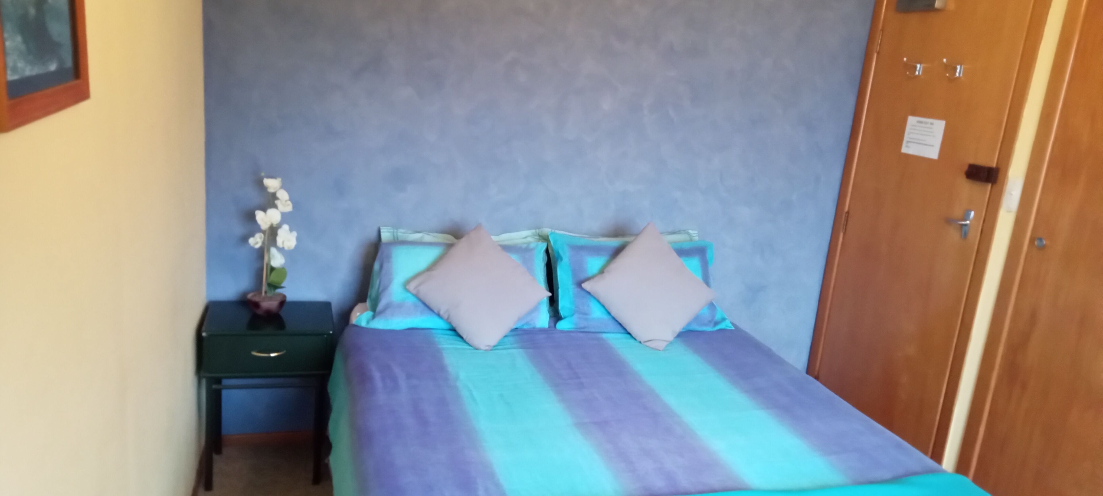 Une chambre à coucher avec un lit, deux oreillers, une table de chevet et un vase de fleurs.