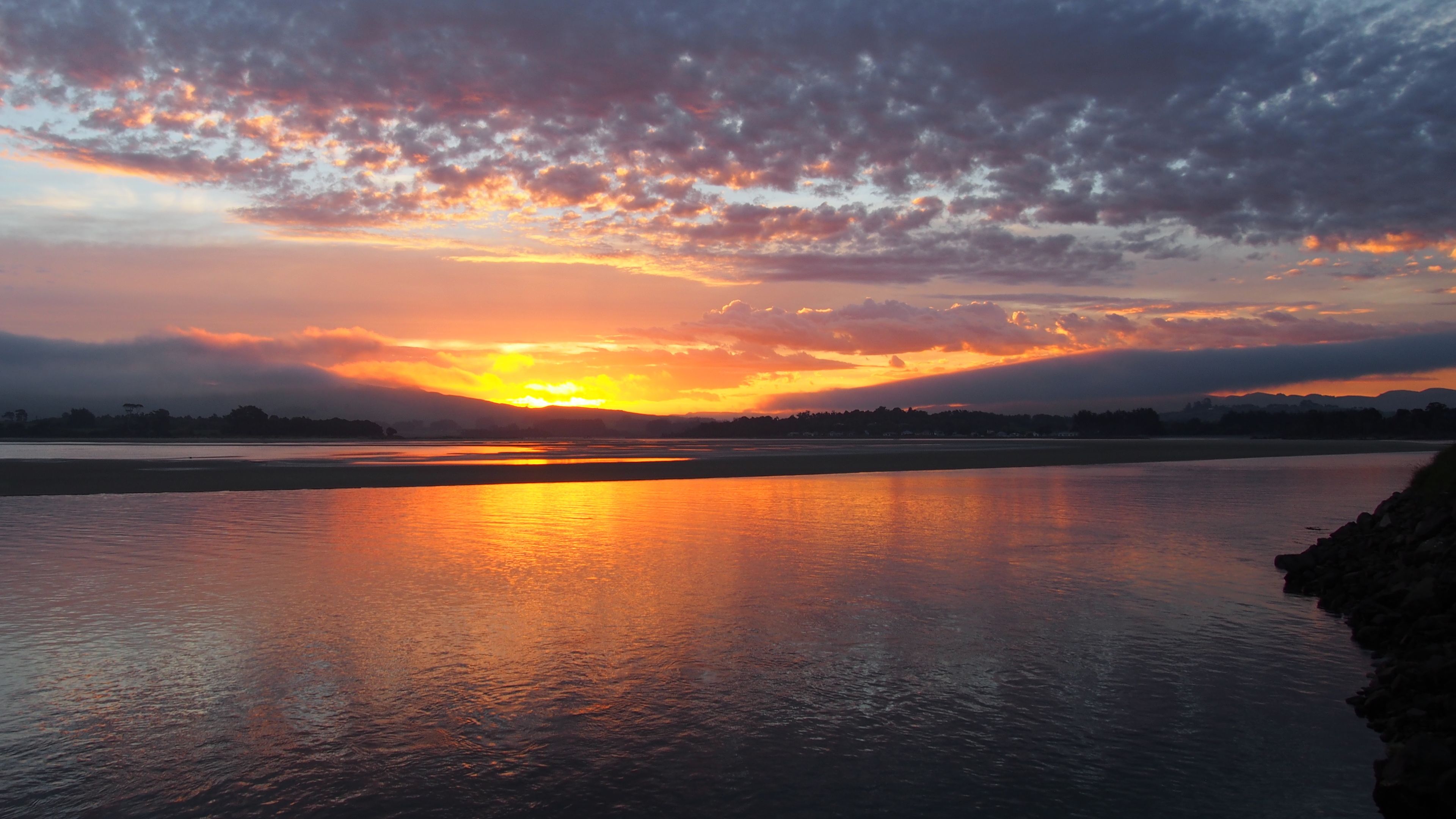A sunset over a calm river with a rocky shoreline.