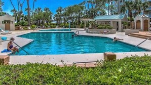 A swimming pool with a clear blue sky, surrounded by palm trees and a building with balconies.