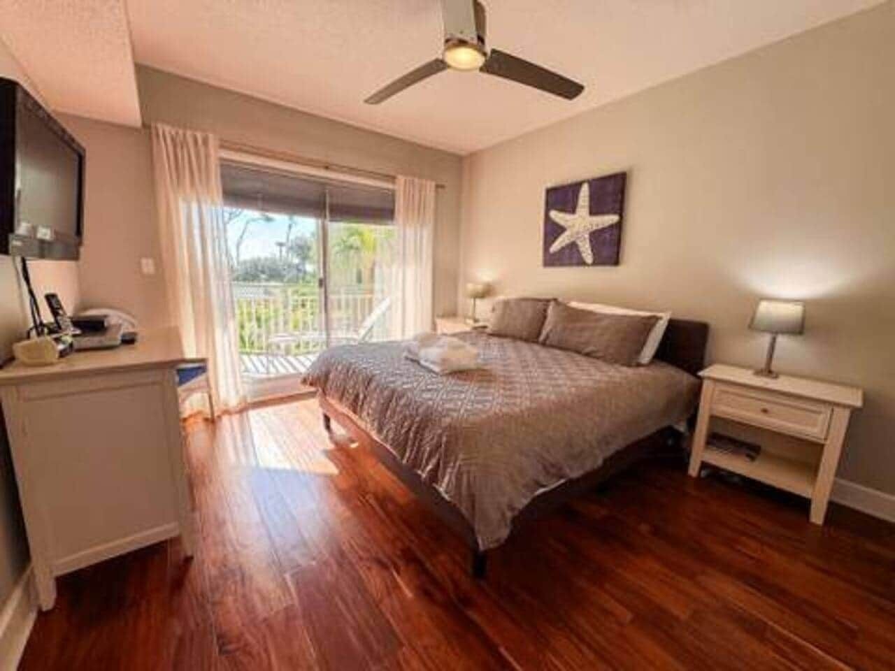 Quarto com cama, escrivaninha, cadeira, ventoinha no teto, janela com cortinas e decoração de estrela-do-mar na parede.