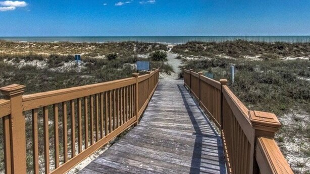 A wooden boardwalk leading to a beach with dunes and a clear sky.