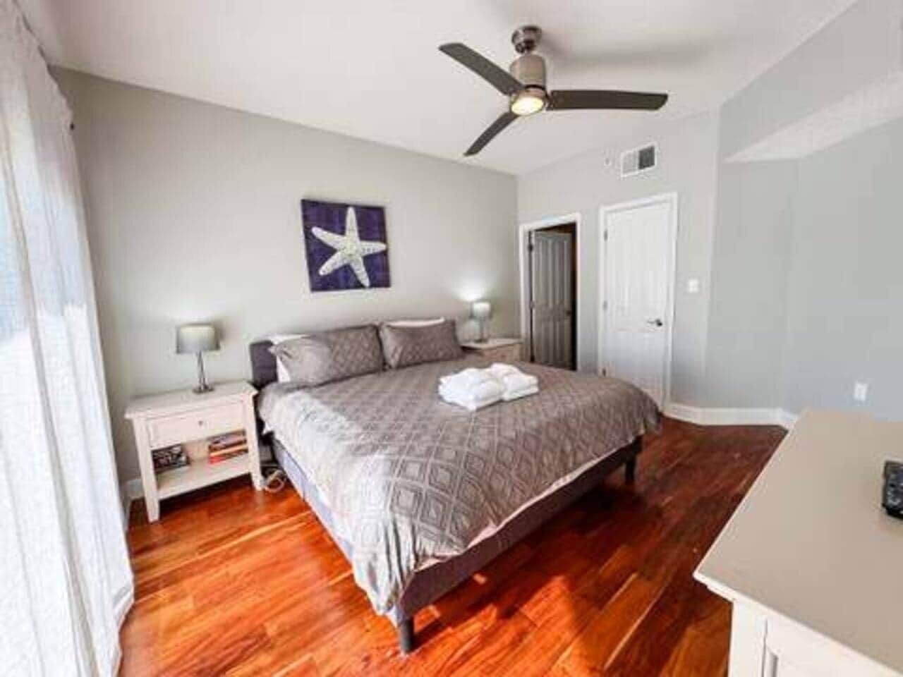 A bedroom with a bed, nightstands, a ceiling fan, a starfish decoration, and a door.