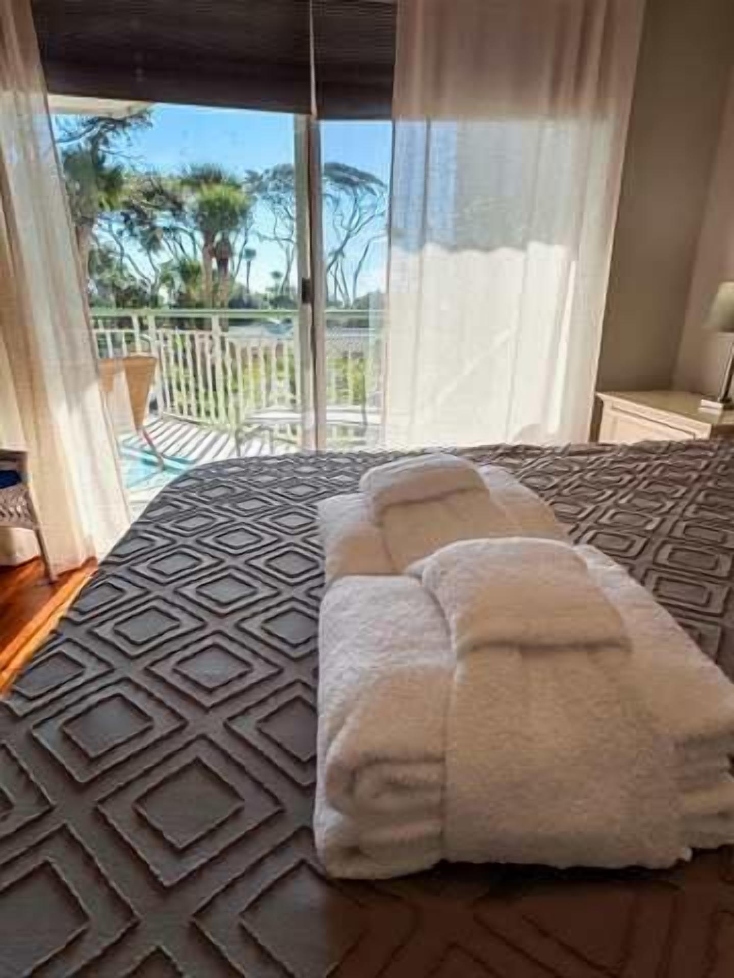 Habitación de hotel con una cama grande, un balcón con vistas a árboles y una ventana con cortinas traslúcidas.