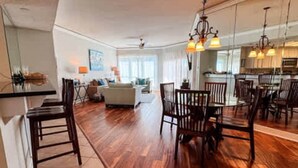 A spacious living area with a dining table and chairs, a sofa, and a kitchen in the background.