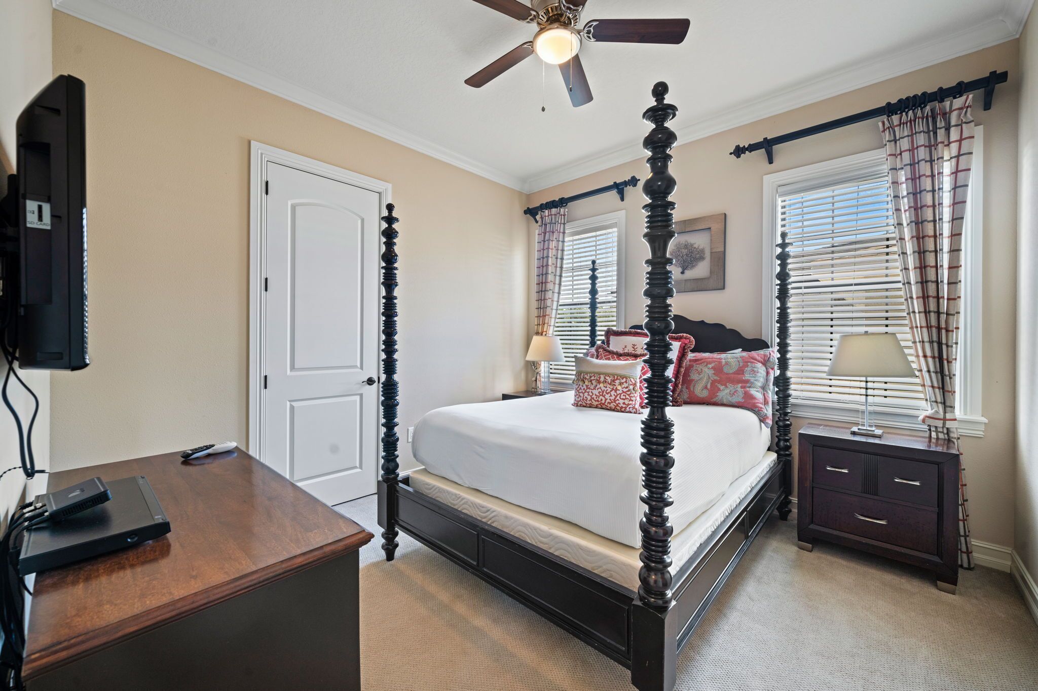 Une chambre à coucher avec un lit à baldaquin, un ventilateur de plafond, une table de chevet avec une lampe et un téléviseur posé sur une commode.
