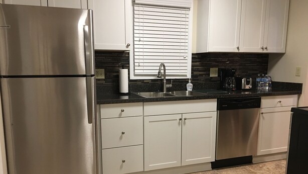 A modern kitchen with white cabinets, stainless steel appliances, a black countertop, and a tiled floor. - Awesome remodeled house! (Mentor)