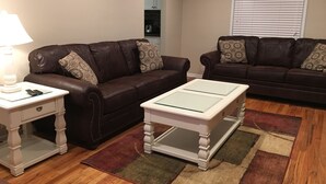 A living room with two brown leather sofas, a white side table, a glass-top coffee table, and a patterned rug. - Awesome remodeled house! (Mentor)
