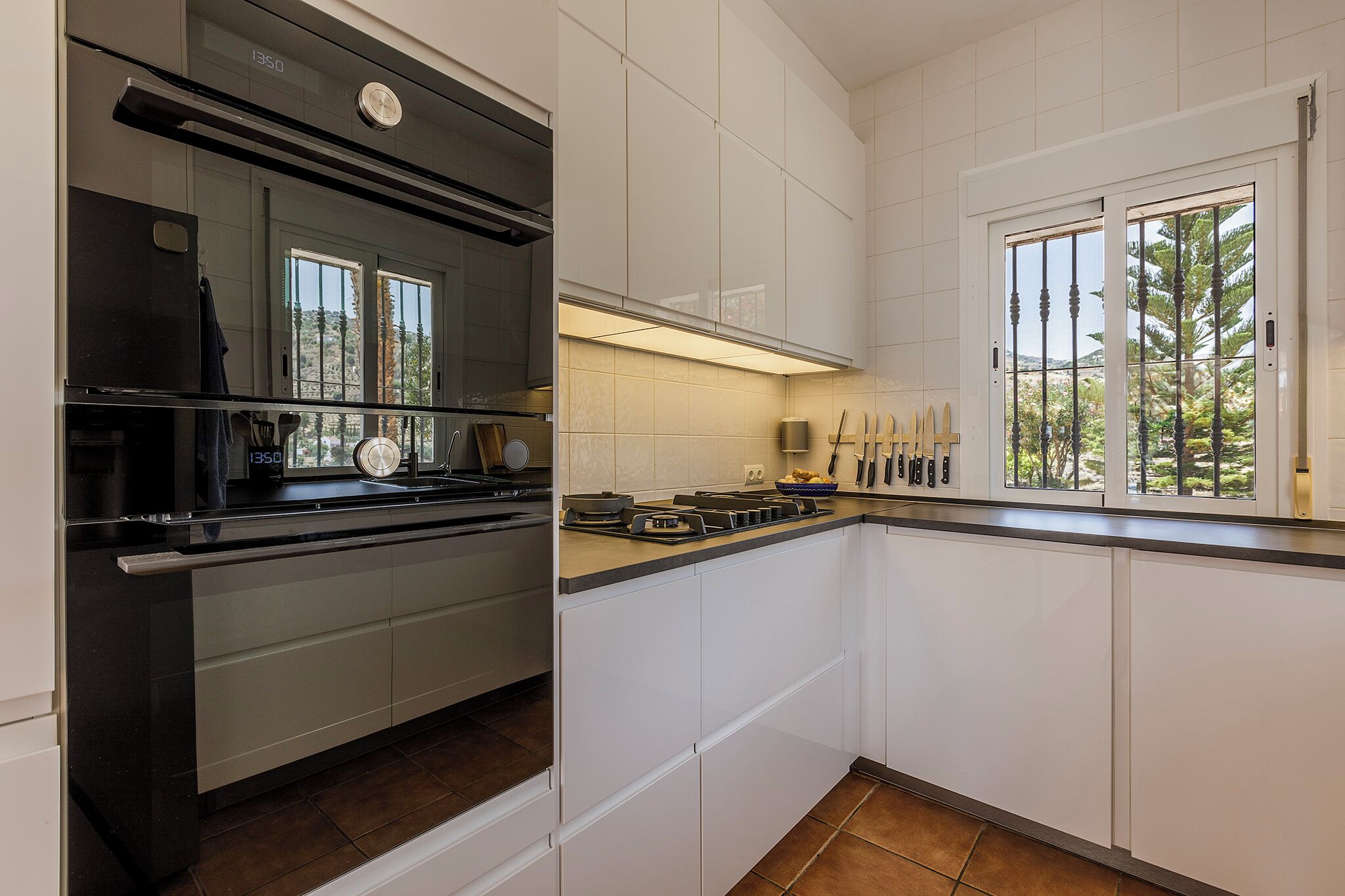 A modern kitchen with white cabinets, a black stove, and a window with a view of trees.