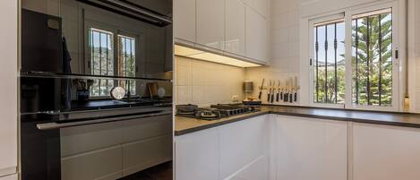 A modern kitchen with white cabinets, a black stove, and a window with a view of trees.