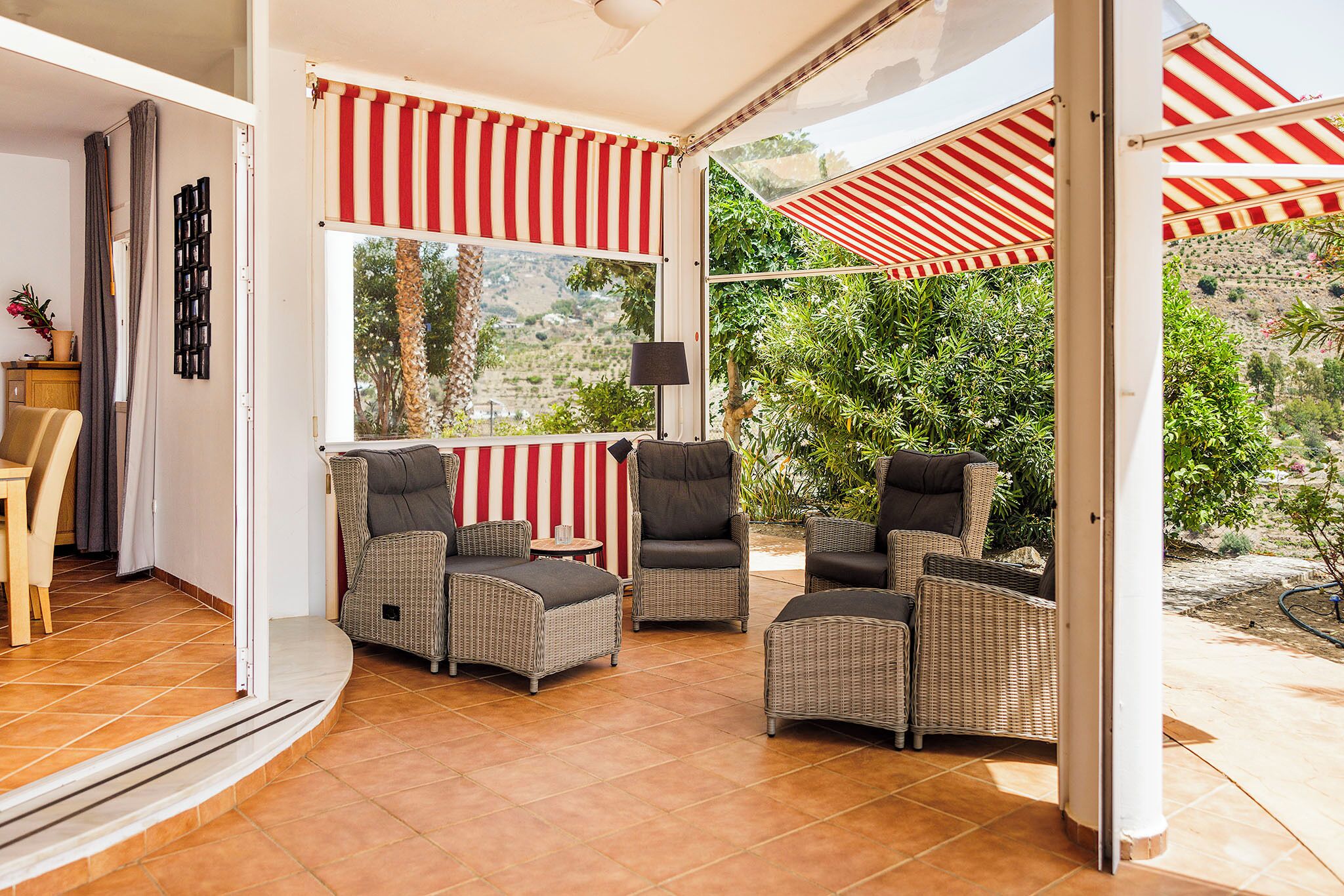 A covered patio with wicker furniture, a view of greenery, and a tiled floor.