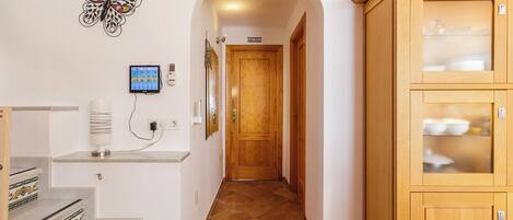 A hallway with a wooden door, a butterfly wall decoration, a digital clock, and a cabinet with glass doors.