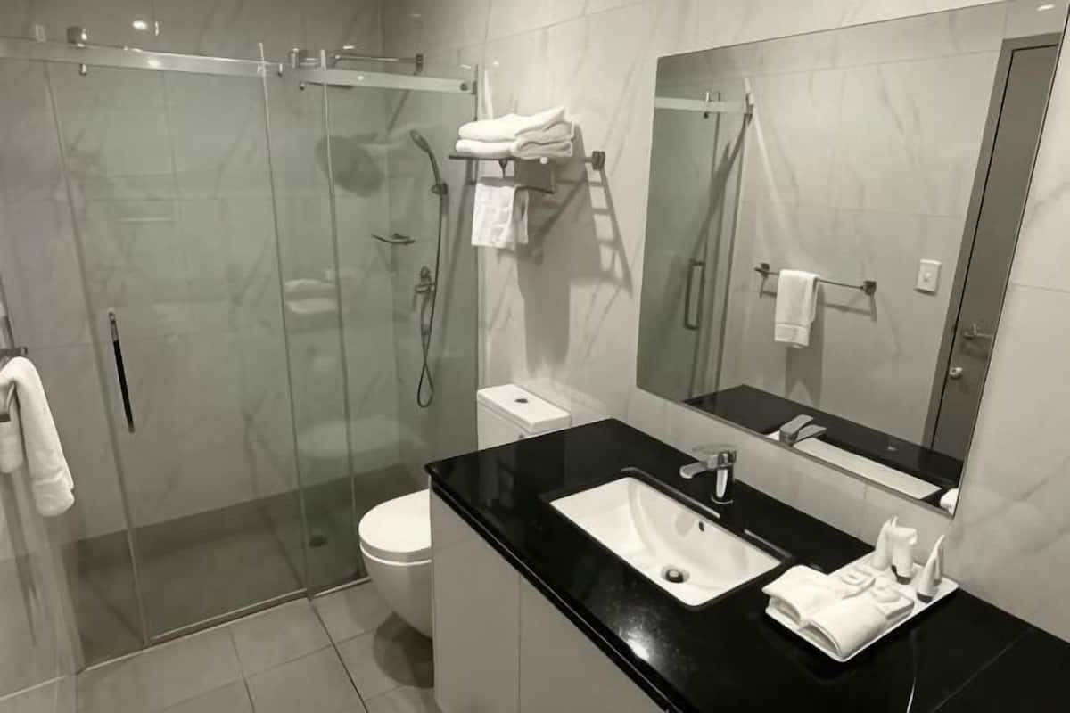 Une salle de bain moderne avec une douche à parois de verre, des toilettes blanches, un lavabo noir et un grand miroir.