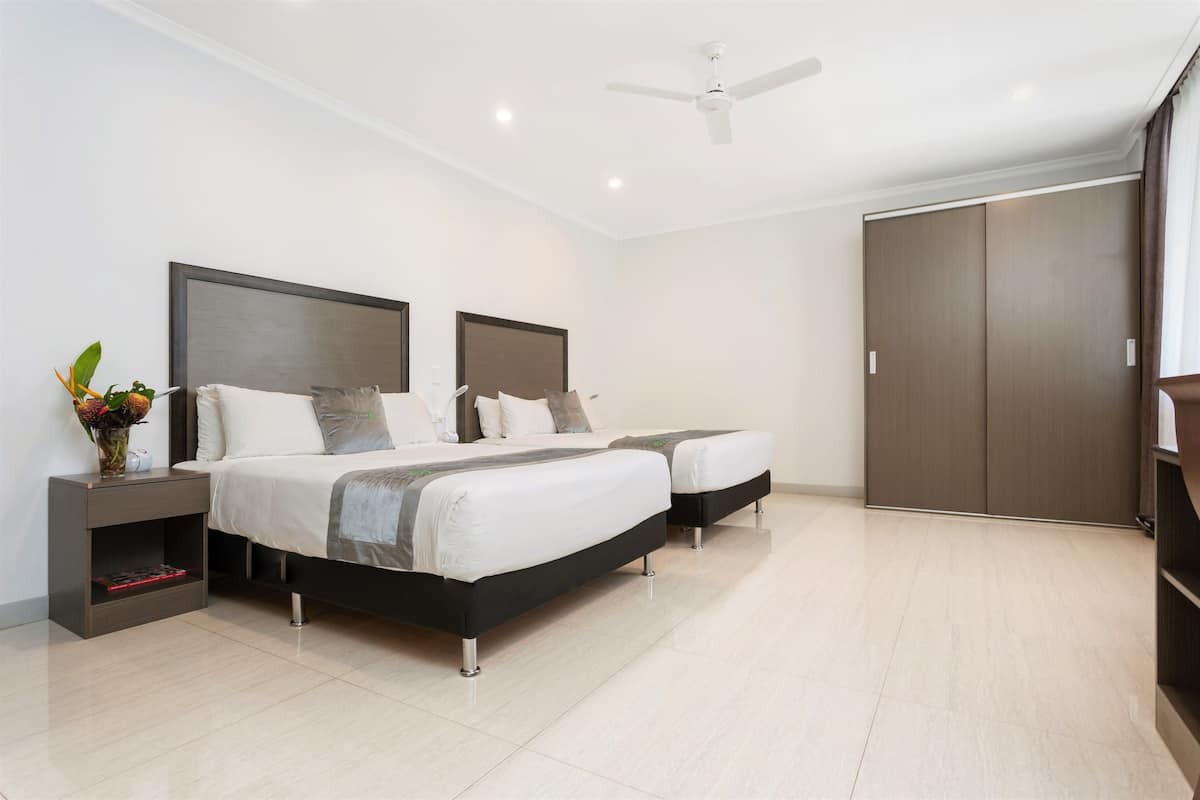 Une chambre moderne avec deux lits, une table de chevet, une commode, un ventilateur de plafond et une armoire.