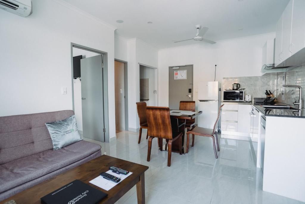 Uma sala moderna com sofá, mesa de jantar com cadeiras, cozinha com micro-ondas e pia, e um ventilador de teto.