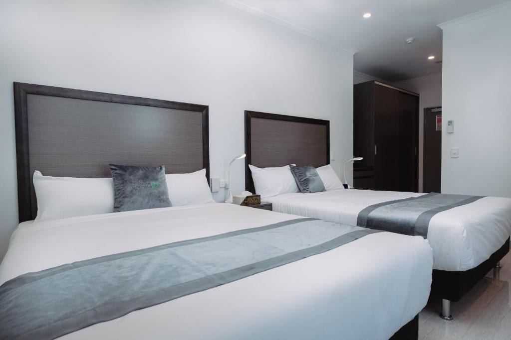 Une chambre d’hôtel avec deux lits, chacun doté d’une tête de lit, de linge de lit blanc et d’une touche de couleur grise.