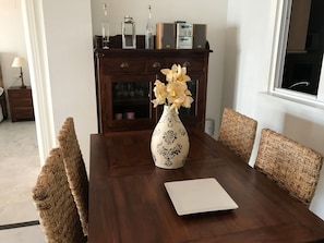 A dining table with a white vase of flowers, a white placemat, and wicker chairs.