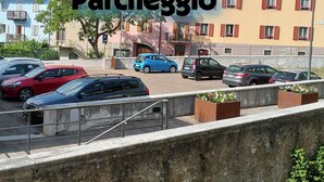 A parking area with several cars, a building with 'Parcheggio' signage, and a stone wall in the foreground.