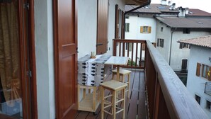 A balcony with a wooden table and two chairs, a wooden door, and a view of neighboring buildings.