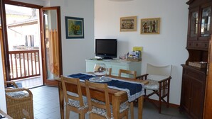 A dining area with a table set for four, a television on a cabinet, and a view of the outside balcony.