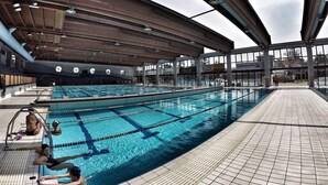Una piscina interior con múltiples carriles, una zona cubierta y un paseo de baldosas.