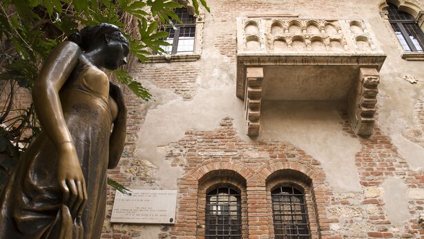 Una estatua de una mujer en un patio con un edificio de ladrillo al fondo.