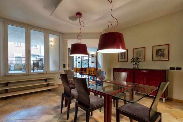 A dining area with a glass table, dark chairs, and red pendant lights. - Large, elegant and comfortable in the center, 20 min. from Lake Garda, 1 hour from Venice (Verona)