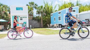 Two people riding bicycles on a street with a small building labeled "Sand Dollar" in the background.