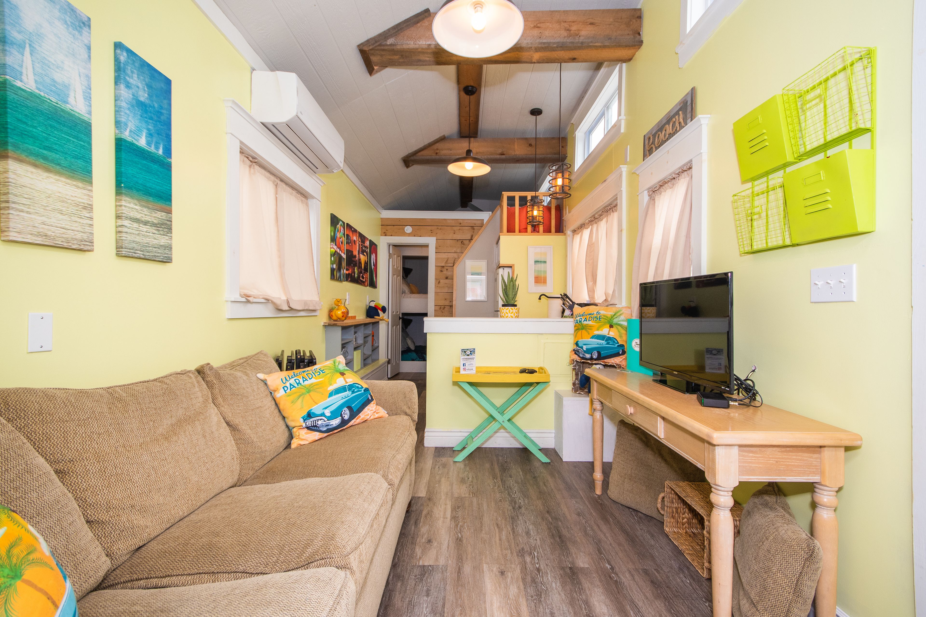 A cozy living room with a sofa, a wooden coffee table, and a TV. There is a kitchen area with a counter and cabinets.