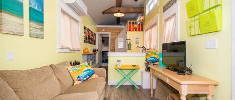A cozy living room with a sofa, a wooden coffee table, and a TV. There is a kitchen area with a counter and cabinets.