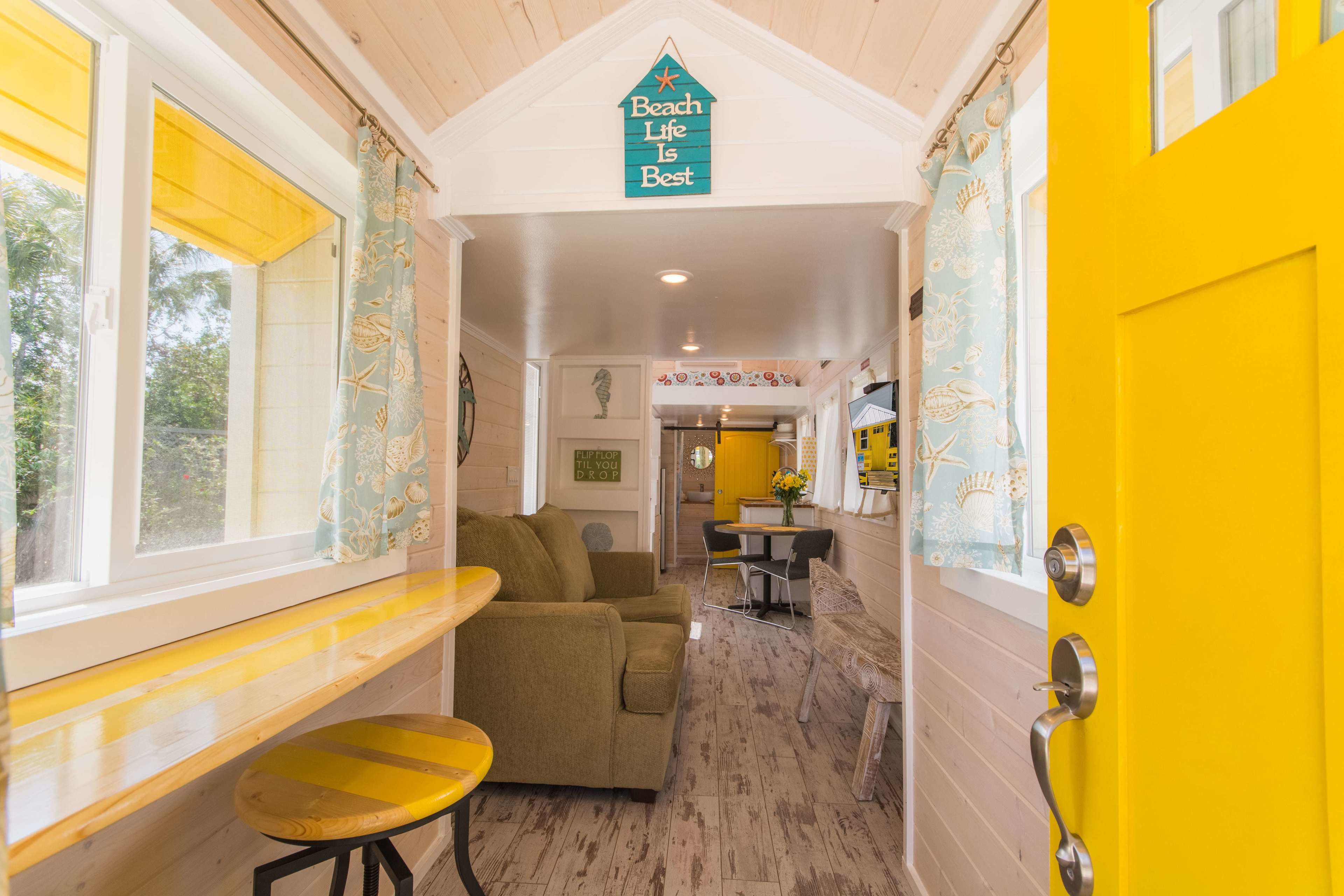 A hallway with a yellow door, a bench, a sofa, and a dining area with a table and chairs.