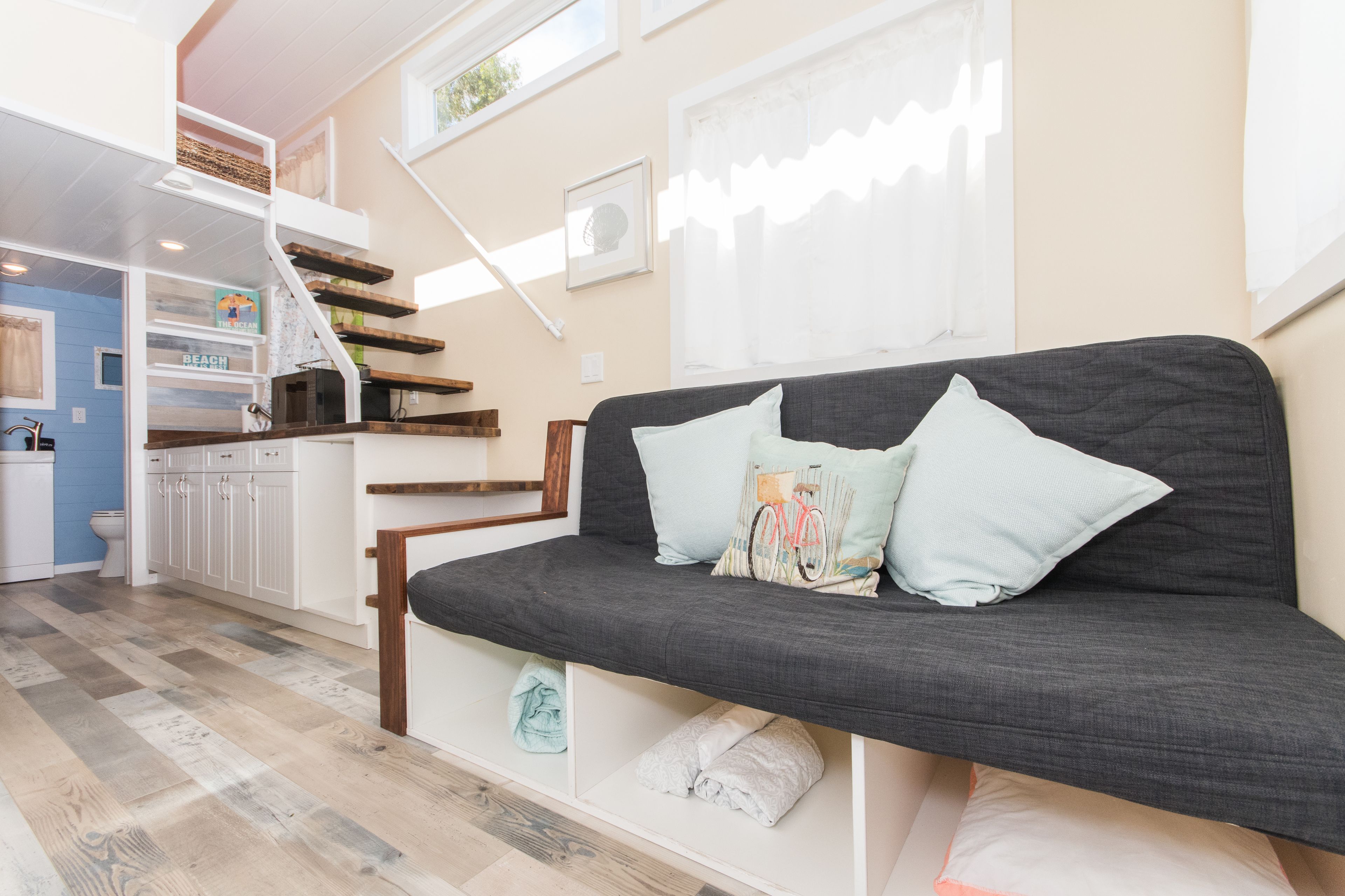 A modern living room with a grey sofa, a staircase, and a kitchen area.