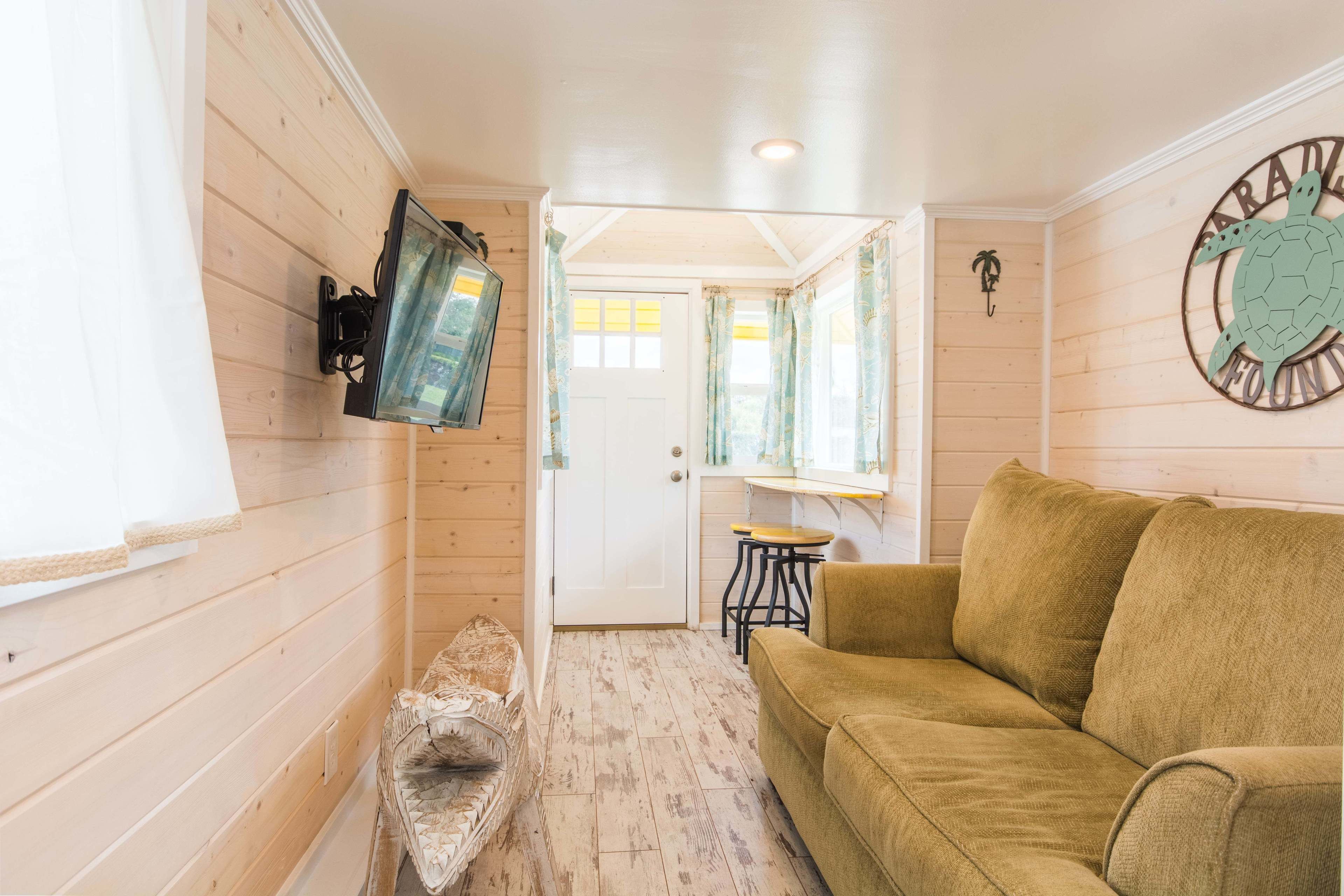 A wooden interior with a sofa, a television mounted on the wall, and a door leading to another room.