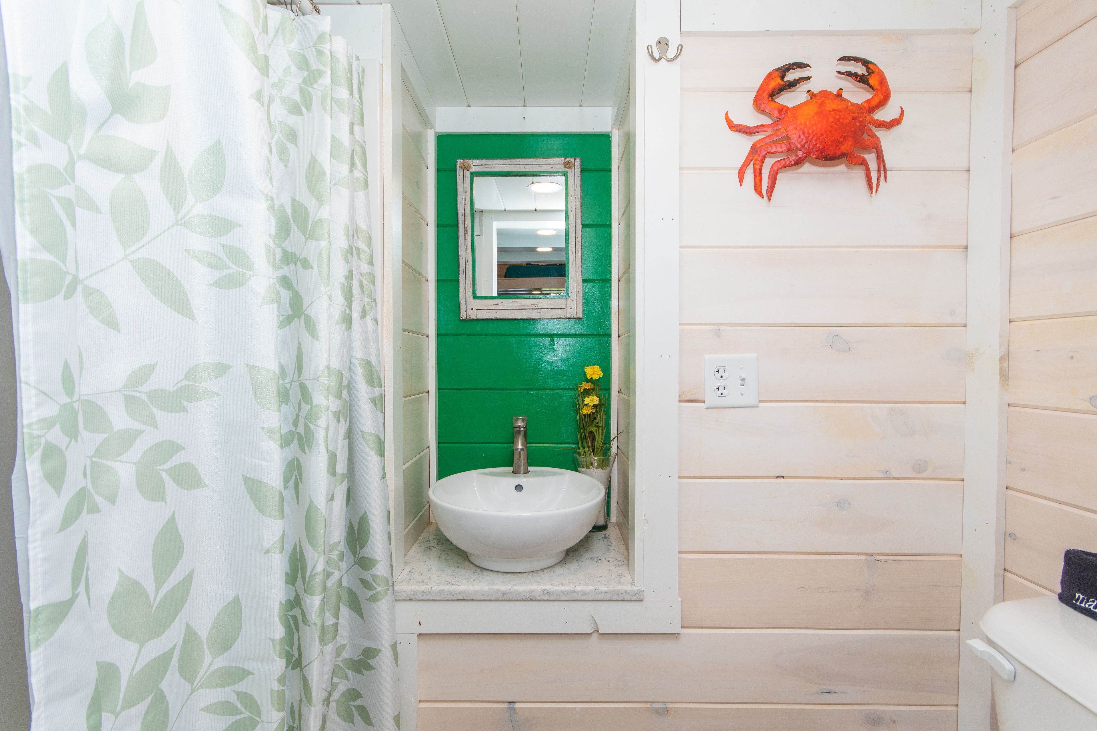 A bathroom with a white sink, green walls, a mirror, and a crab decoration.