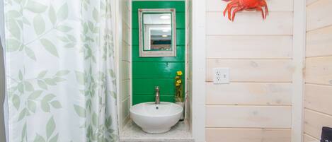 A bathroom with a white sink, green walls, a mirror, and a crab decoration.