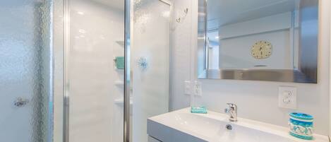A modern bathroom with a glass shower enclosure, a white sink, and a large mirror.