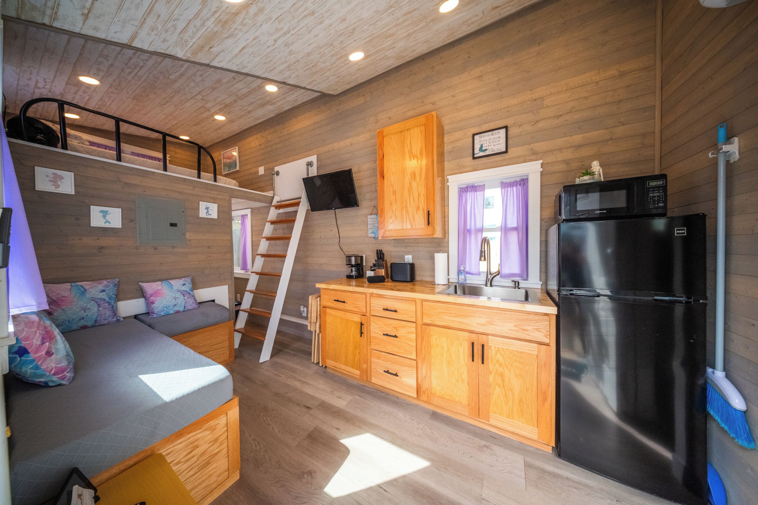 A compact kitchen with wooden cabinets, a refrigerator, a microwave, and a sink.