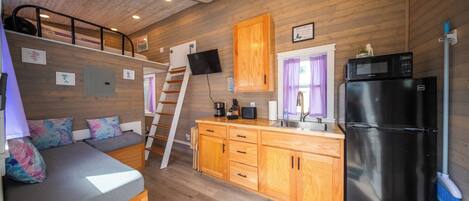 A compact kitchen with wooden cabinets, a refrigerator, a microwave, and a sink.
