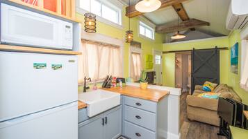 A compact kitchen with a microwave, sink, and wooden countertop.