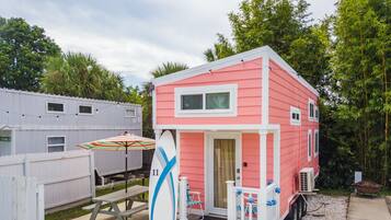 A pink mobile home with a small porch and a surfboard leaning against it.