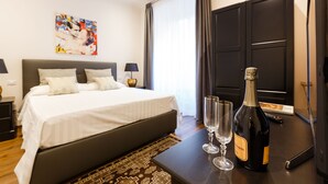 A hotel room with a large bed, two bedside tables with lamps, a bottle of champagne, and two glasses on the nightstand.