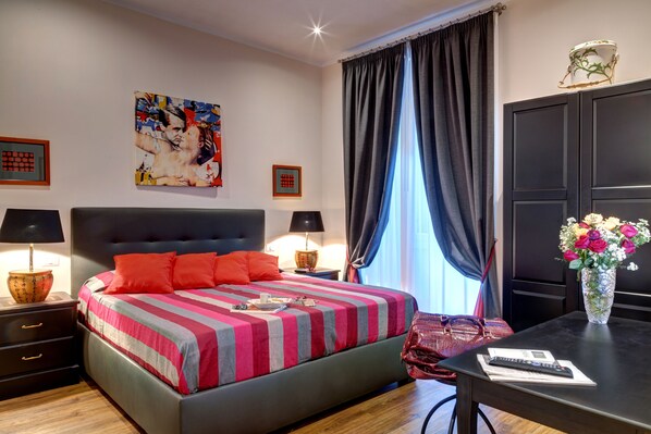 A modern hotel room with a large bed, two bedside tables with lamps, a desk with a vase of flowers, and a painting on the wall. - ROME BOUTIQUE APARTMENTS comfortable, cozy, central, 8minutes from the vatican (Roma)