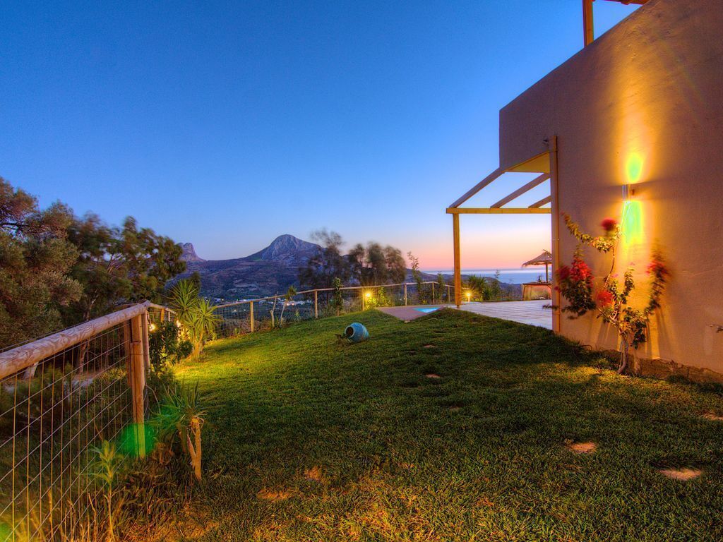 Une pelouse bien entretenue, une clôture en bois, une pergola illuminée de guirlandes lumineuses et une montagne en arrière-plan.