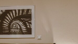 Een net opgemaakt bed met een bedsprei en kussens met een patroon, een ingelijste foto aan de muur en een bedlampje.