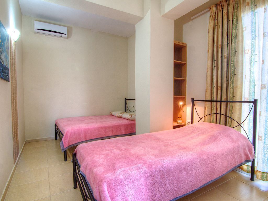Une chambre avec deux lits simples, un appareil de climatisation, une table de chevet avec une lampe et une fenêtre avec des rideaux.